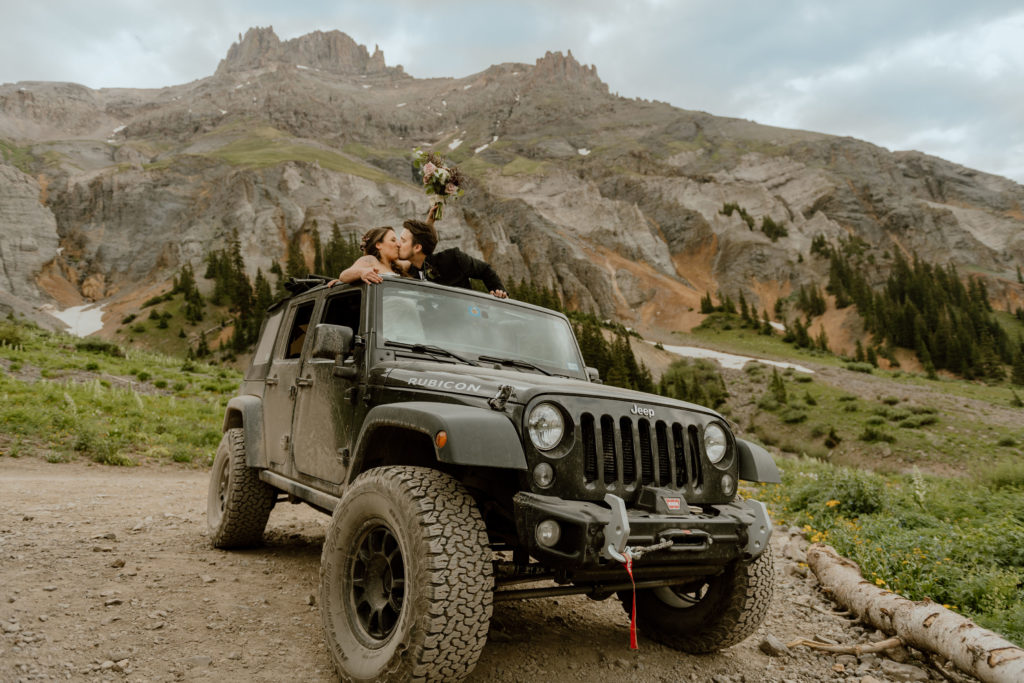 Just married couple standing in Jeep sharing a kiss in the San Juan Mountains above Ouray, Colorado.